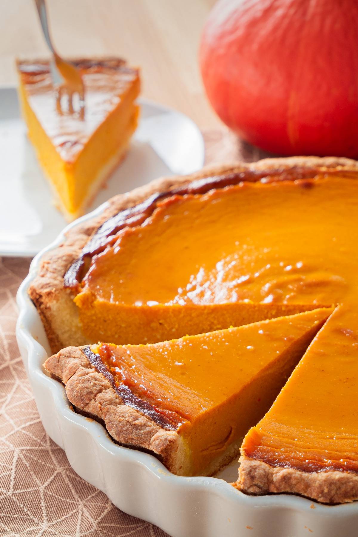 Leckeres Pumpkin Pie Rezept – Der amerikanische Klassiker Ein Stück cremiger Pumpkin Pie auf einem Teller, mit einem Hokkaido-Kürbis und der restlichen Tarte im Vordergrund.