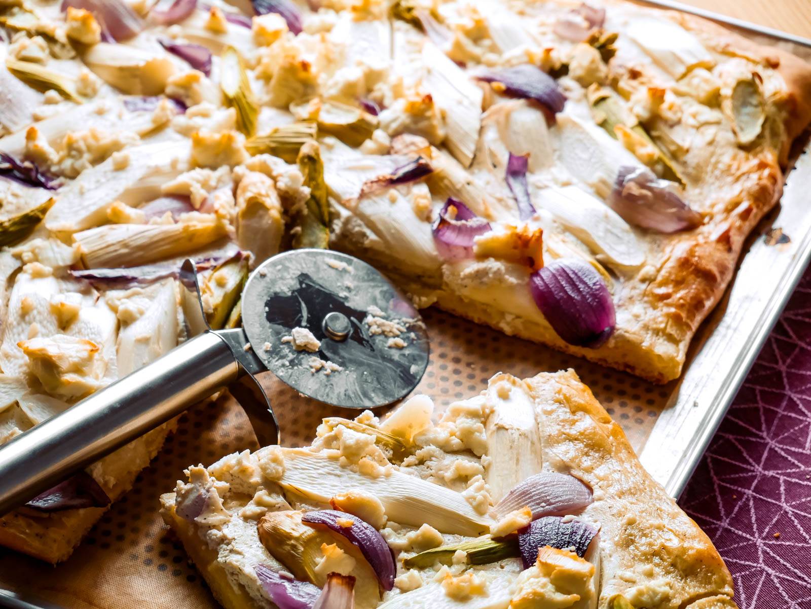 Ein Stück herzhafter Spargelkuchen mit Spargelspitzen und Käse, auf einem Backblech.