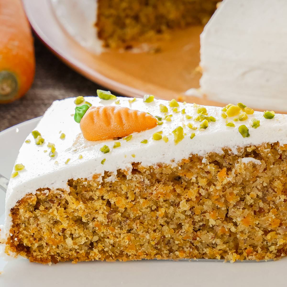 Karottenkuchen mit Frischkäse-Frosting Ein saftiges Stück Karottenkuchen, bedeckt mit Frischkäse-Frosting und dekoriert mit einer Karottenfigur, serviert auf einem weißen Teller.