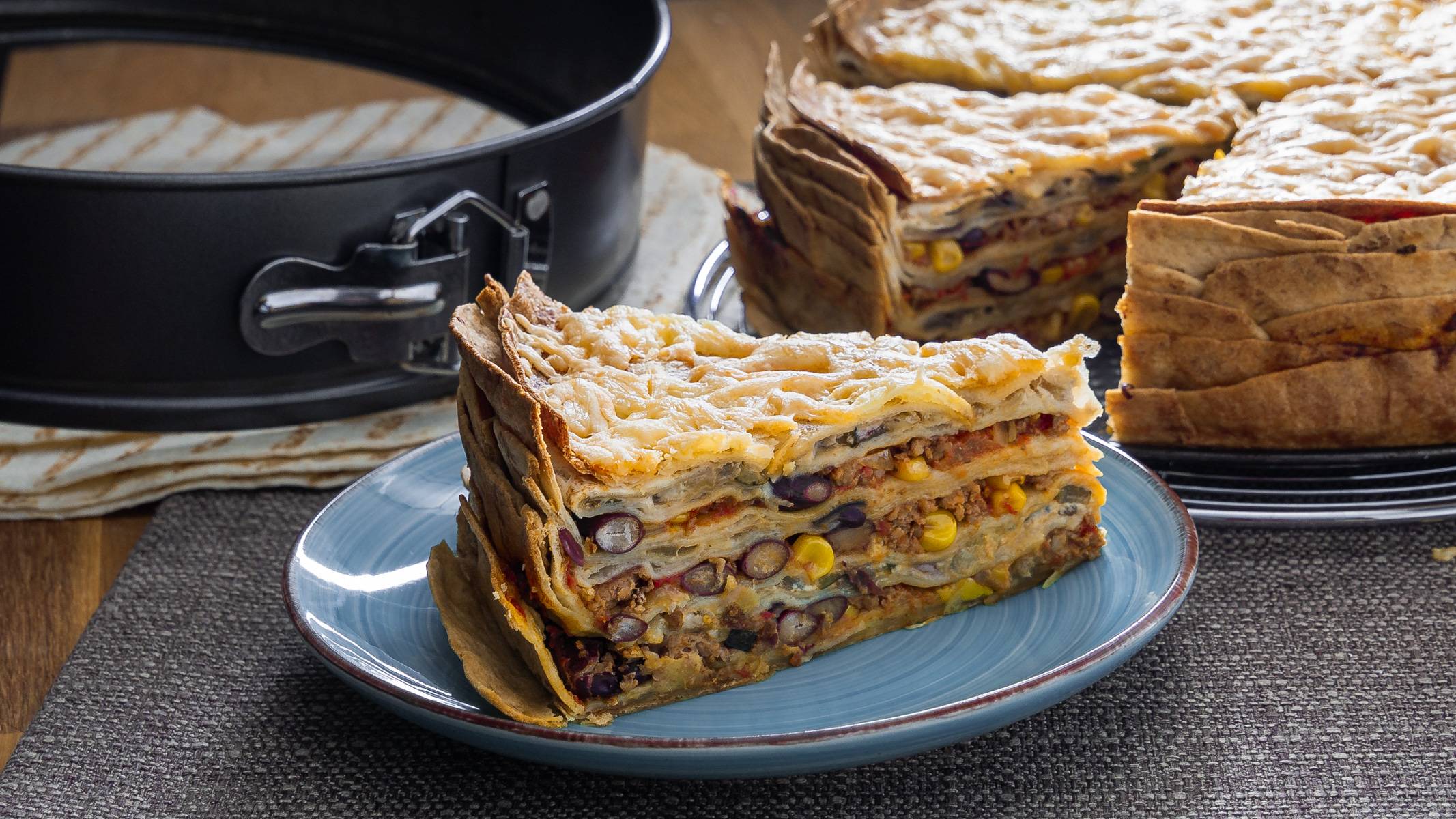Mexikanische Tortilla Lasagne – Der perfekte Wrap Auflauf für alle Tex-Mex-Fans! Herzhafte Mexikanische Tortilla Lasagne mit einer goldenen Käseschicht, serviert auf einem blauen Teller.