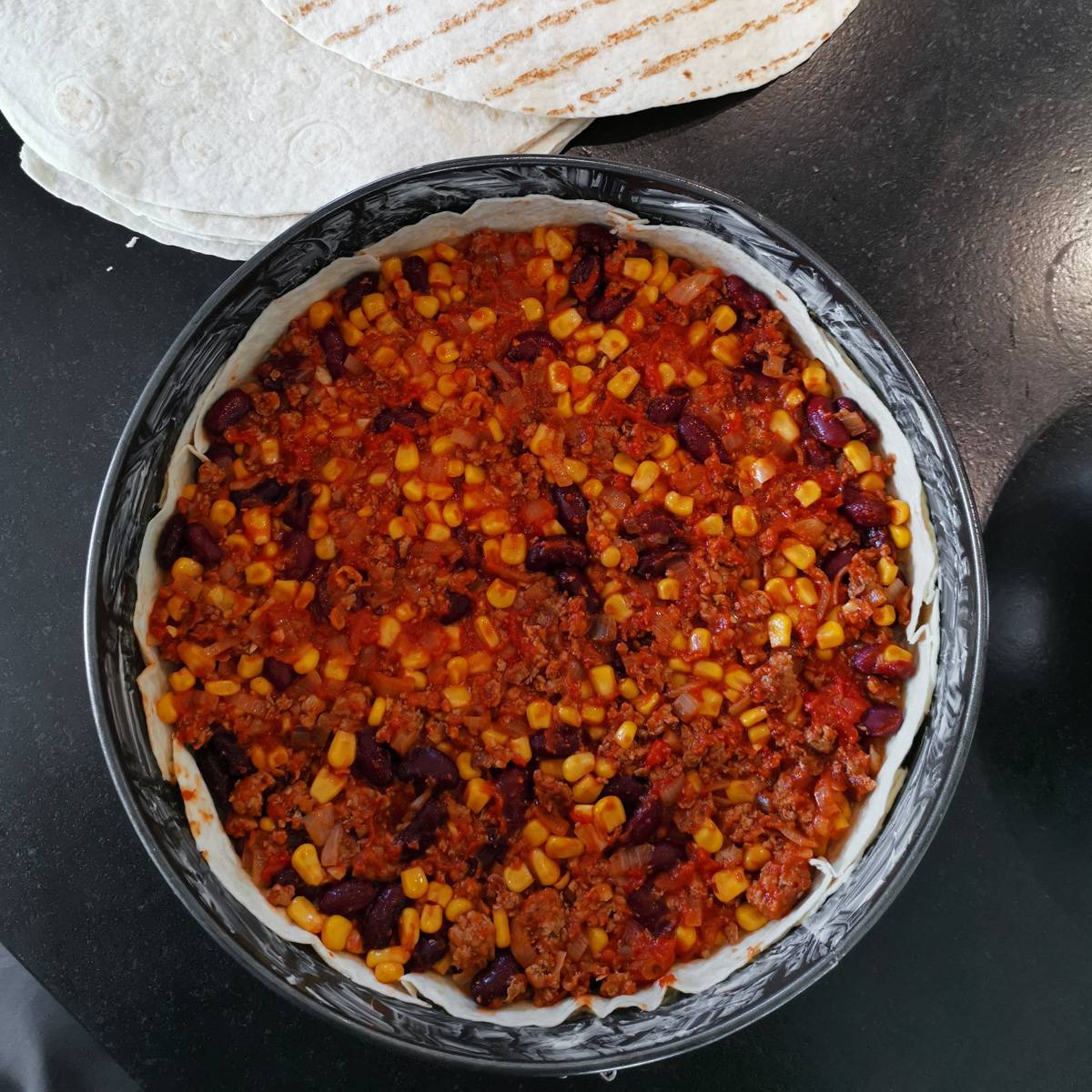 Mexikanische Tortilla Lasagne – Der perfekte Wrap Auflauf für alle Tex-Mex-Fans! Die Tex-Mex-Füllung mit Hackfleisch, Bohnen und Mais wird gleichmäßig auf die Tortillas in der Springform verteilt.